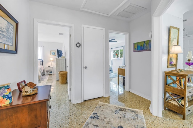 hallway featuring visible vents, baseboards, attic access, and speckled floor