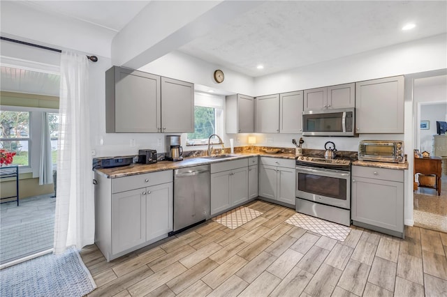 kitchen with wood tiled floor, a toaster, gray cabinets, a sink, and appliances with stainless steel finishes