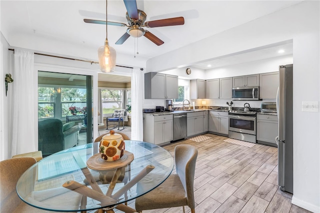 kitchen featuring wood finish floors, a ceiling fan, gray cabinets, a sink, and appliances with stainless steel finishes