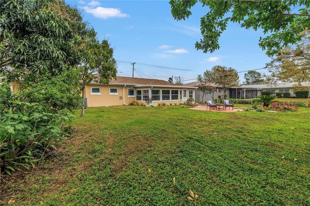 rear view of property with a patio area, a lawn, a sunroom, and stucco siding