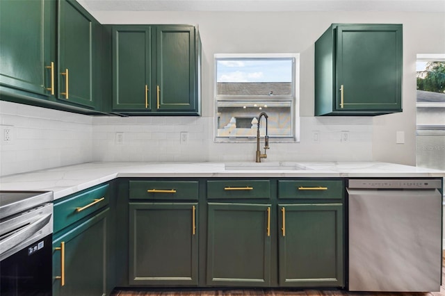 kitchen with stainless steel appliances, a sink, green cabinets, and tasteful backsplash