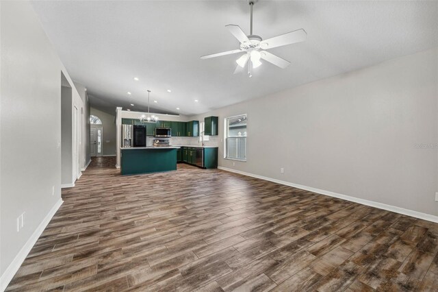 unfurnished living room with ceiling fan with notable chandelier, dark wood-style flooring, recessed lighting, and baseboards