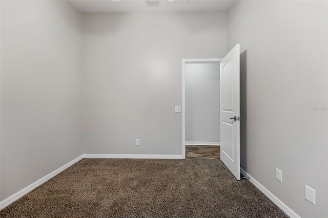 unfurnished room with baseboards and dark carpet