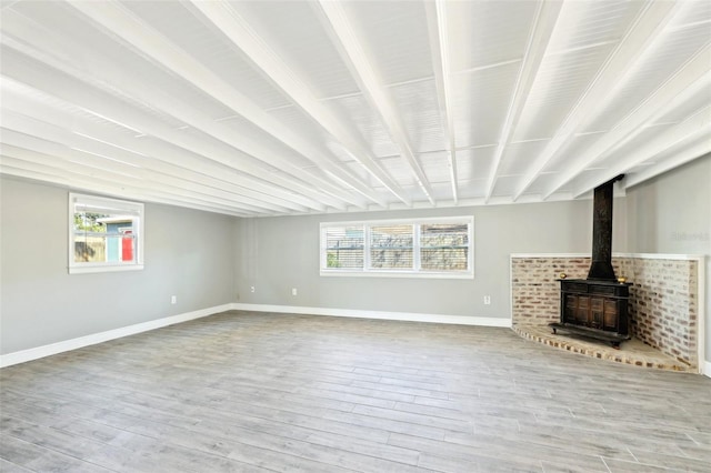 unfurnished living room featuring wood finished floors, a wood stove, and baseboards