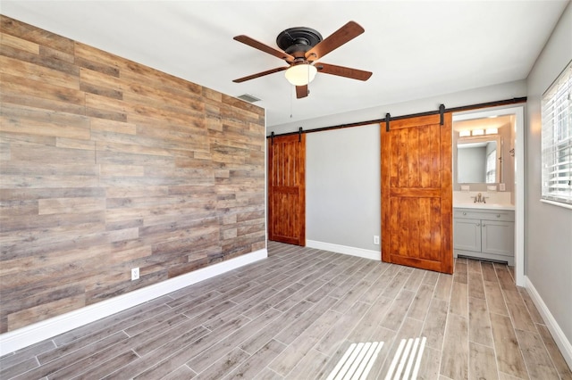 unfurnished bedroom featuring light wood finished floors, a barn door, visible vents, and wood walls