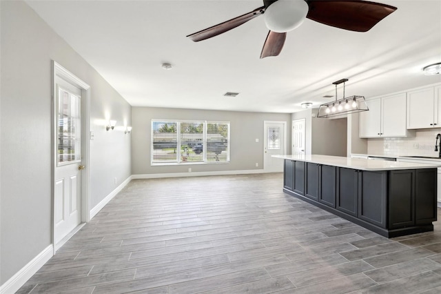 kitchen featuring white cabinetry, open floor plan, light countertops, light wood finished floors, and tasteful backsplash