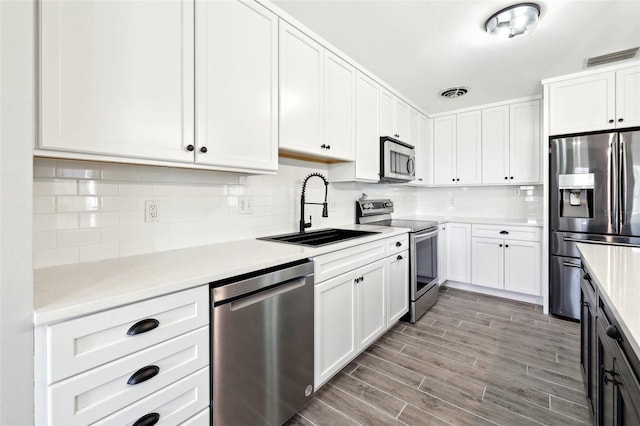 kitchen with stainless steel appliances, a sink, white cabinets, light countertops, and tasteful backsplash