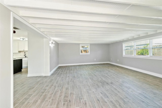 unfurnished room with light wood-style floors, baseboards, and beamed ceiling