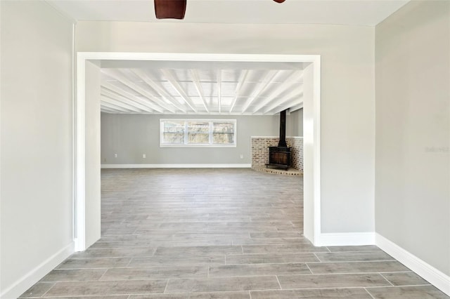 unfurnished living room with a wood stove, ceiling fan, baseboards, and wood finished floors