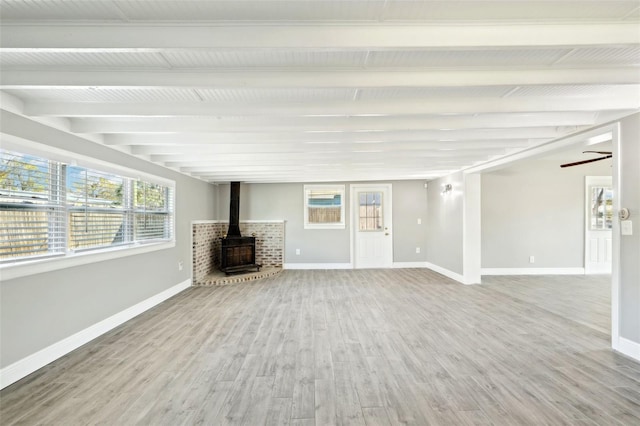 unfurnished living room with a wood stove, ceiling fan, baseboards, and wood finished floors