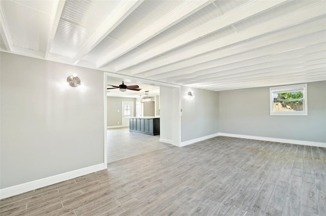 spare room featuring light wood-type flooring, baseboards, and beam ceiling