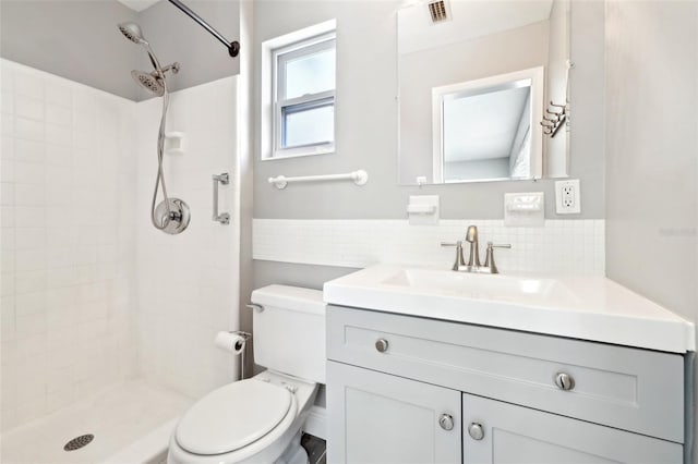 bathroom with toilet, vanity, visible vents, a tile shower, and backsplash