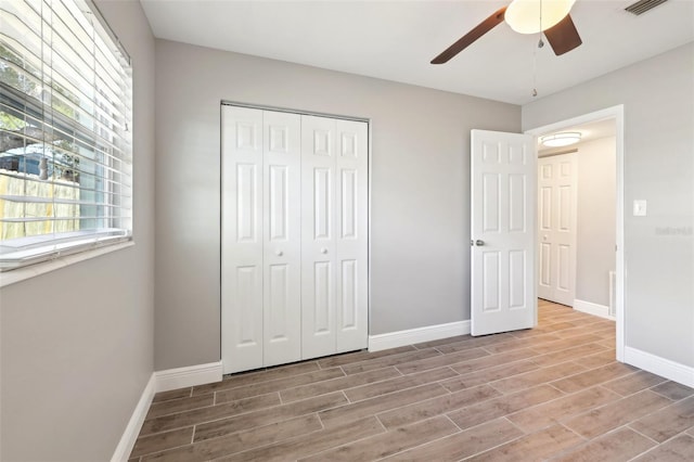 unfurnished bedroom with a closet, visible vents, a ceiling fan, wood finished floors, and baseboards