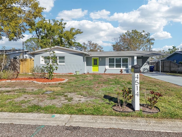 ranch-style house featuring a front lawn, fence, an attached carport, and concrete driveway