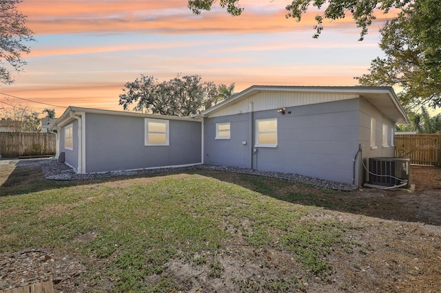 back of house at dusk featuring a lawn, cooling unit, and fence