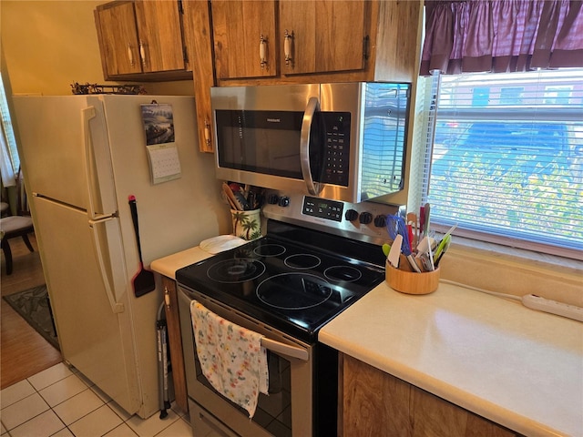 kitchen featuring brown cabinets, light tile patterned floors, stainless steel appliances, and light countertops