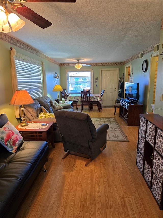 living area featuring light wood-style floors, ceiling fan, visible vents, and a textured ceiling