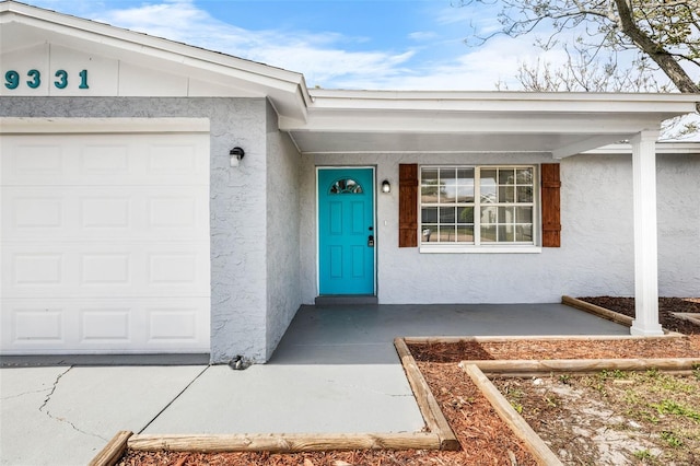 view of exterior entry with a garage and stucco siding