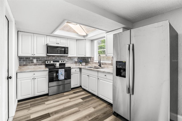 kitchen with white cabinets, light wood-style flooring, stainless steel appliances, and a sink