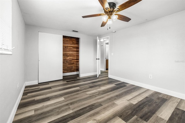 unfurnished bedroom with a closet, visible vents, a ceiling fan, wood finished floors, and baseboards