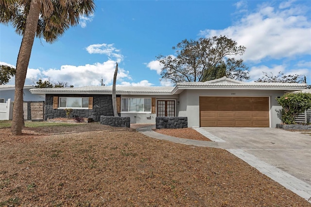 ranch-style house with an attached garage, fence, driveway, stone siding, and stucco siding