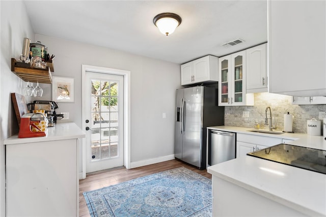 kitchen featuring stainless steel appliances, visible vents, decorative backsplash, glass insert cabinets, and a sink