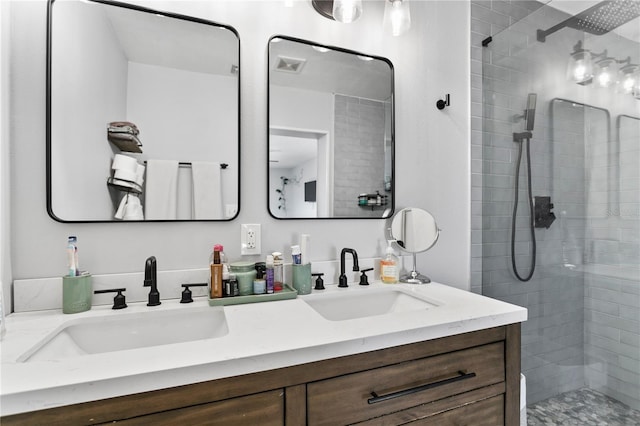 full bath with double vanity, tiled shower, a sink, and visible vents