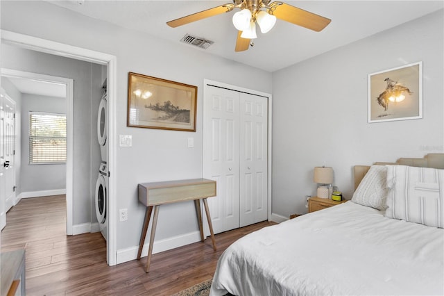 bedroom featuring baseboards, visible vents, stacked washer and clothes dryer, dark wood-type flooring, and a closet