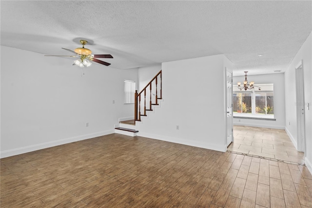 unfurnished living room featuring stairs, ceiling fan with notable chandelier, a textured ceiling, and wood finished floors