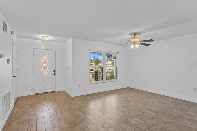 foyer entrance with visible vents, a textured ceiling, baseboards, and wood finished floors