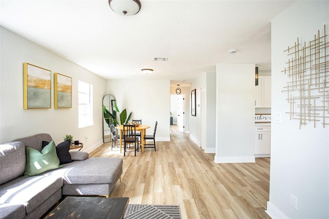 living room featuring light wood-type flooring, visible vents, and baseboards