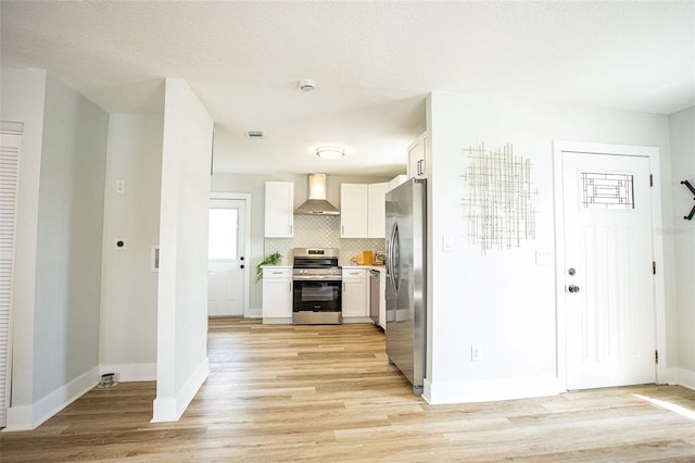 kitchen with light wood-style flooring, backsplash, appliances with stainless steel finishes, white cabinets, and wall chimney exhaust hood