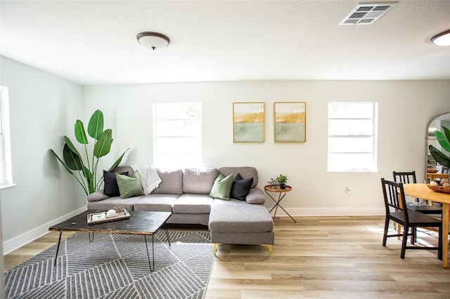 living area featuring light wood-style flooring, plenty of natural light, and visible vents