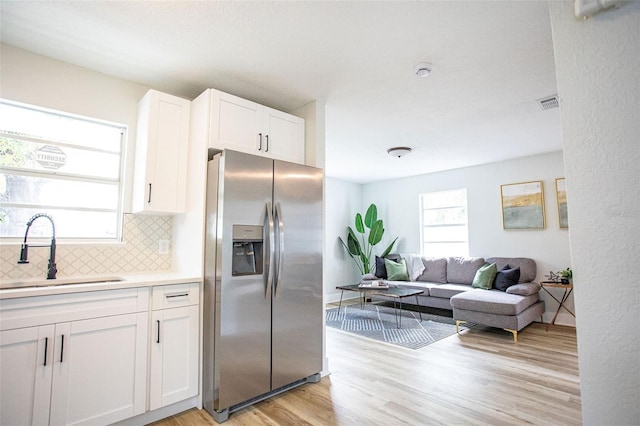 kitchen featuring a healthy amount of sunlight, backsplash, stainless steel refrigerator with ice dispenser, and a sink