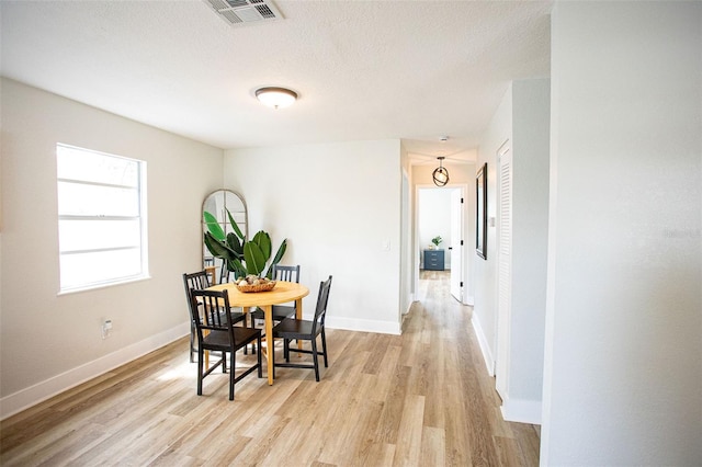 dining room with visible vents, light wood-style flooring, baseboards, and a textured ceiling