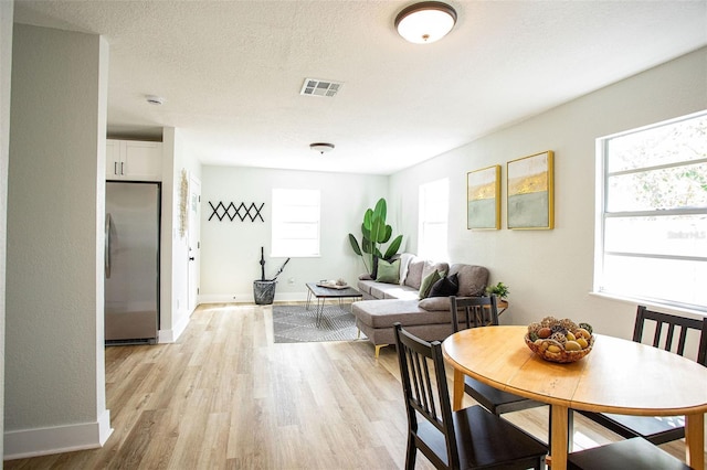 dining space with baseboards, visible vents, a textured ceiling, and light wood finished floors