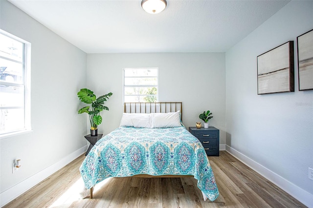 bedroom with multiple windows, wood finished floors, and baseboards