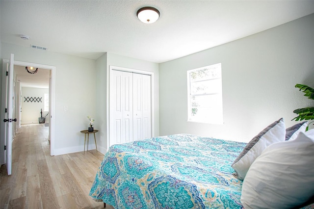 bedroom with a textured ceiling, visible vents, baseboards, light wood-style floors, and a closet