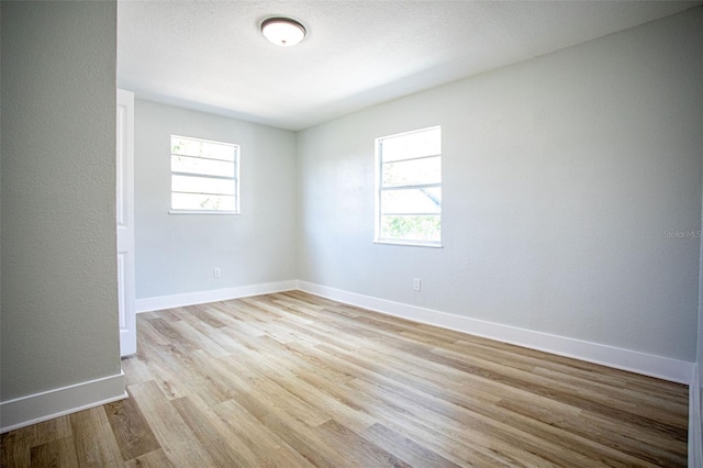 empty room with wood finished floors, a wealth of natural light, and baseboards