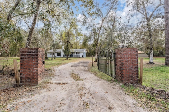 view of street with dirt driveway, a gate, and a gated entry