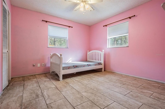 unfurnished bedroom with a textured ceiling, light tile patterned floors, multiple windows, and a closet