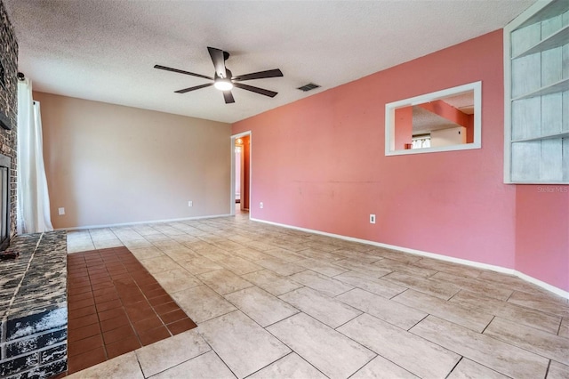 empty room featuring a fireplace, visible vents, a ceiling fan, a textured ceiling, and baseboards