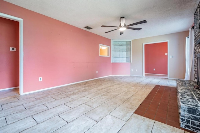 empty room with a textured ceiling, visible vents, baseboards, a ceiling fan, and a brick fireplace