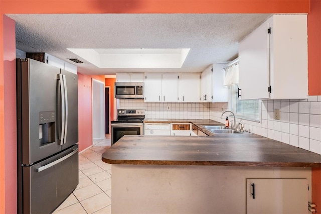 kitchen with light tile patterned floors, a peninsula, a sink, appliances with stainless steel finishes, and dark countertops