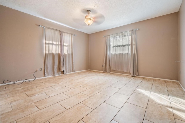 empty room with a textured ceiling, a ceiling fan, a wealth of natural light, and light tile patterned flooring