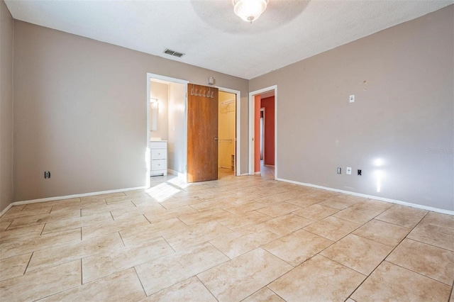 unfurnished bedroom featuring a closet, visible vents, connected bathroom, a textured ceiling, and baseboards