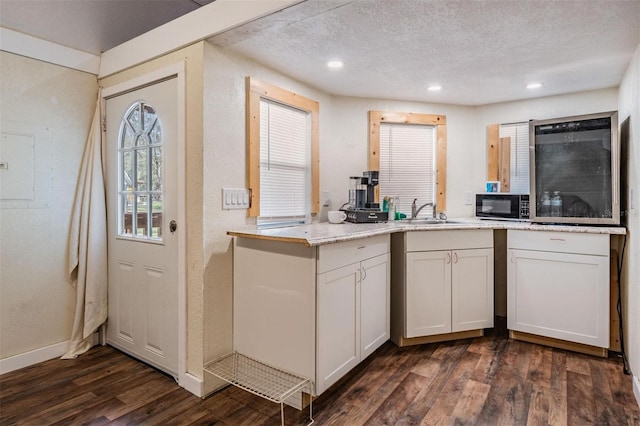 kitchen with a textured ceiling, a textured wall, a sink, white cabinetry, and dark wood-style floors