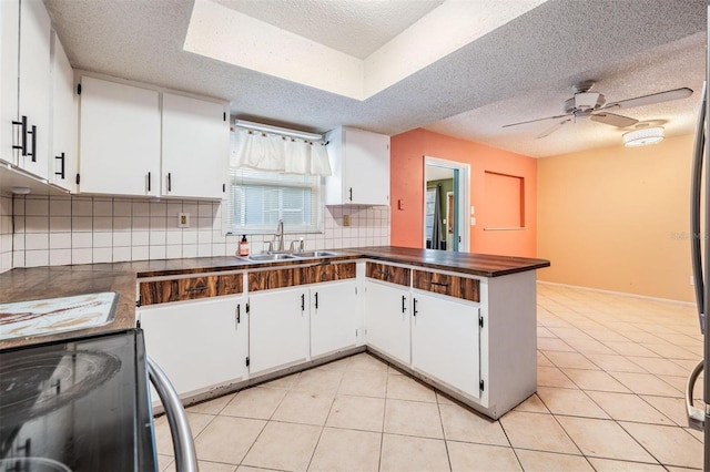 kitchen with dark countertops, a peninsula, black electric range, a sink, and light tile patterned flooring