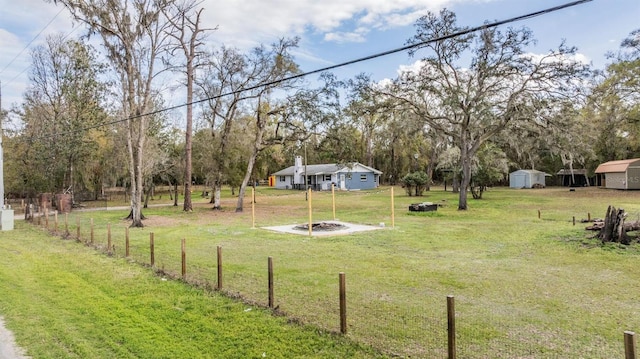 view of yard featuring a storage shed, an outdoor fire pit, an outdoor structure, and fence