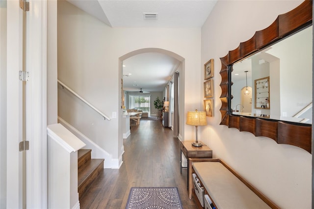 hallway with arched walkways, dark wood-style flooring, visible vents, stairway, and baseboards